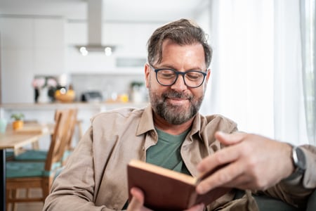 Lächelnder reifer Mann, der zu Hause ein Buch liest iStock-2215393306