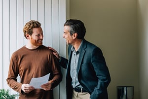 Lächelnder junger Mann und älterer Mann mit Dokumentdiskussion im Büro iStock-2087206093