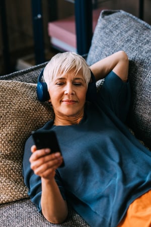 Podcast - Seniorin hört Musik mit Telefon und Kopfhörern iStock-1790914440