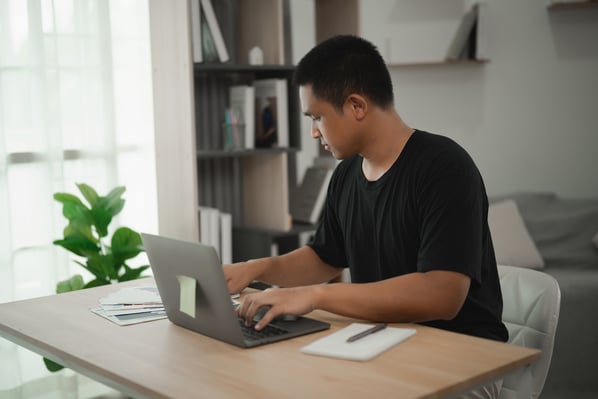 Junger Mann, der an einem Laptop an einem modernen Schreibtisch im hellen Homeoffice arbeitet iStock-2228589750