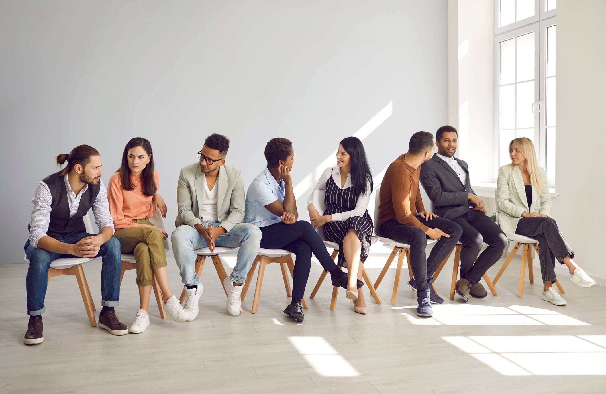 bunt gemischte Gruppe , die in einer Sitzreihe sitzt miteinander sprechen iStock-2212131982
