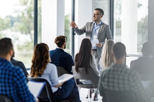 Hero_ Happy business leader talking to group of his colleagues on a seminar in board roomiStock-2116544916