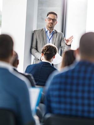 Männlicher Geschäftsführer spricht mit einer Gruppe seiner Kollegen iStock-1959561203