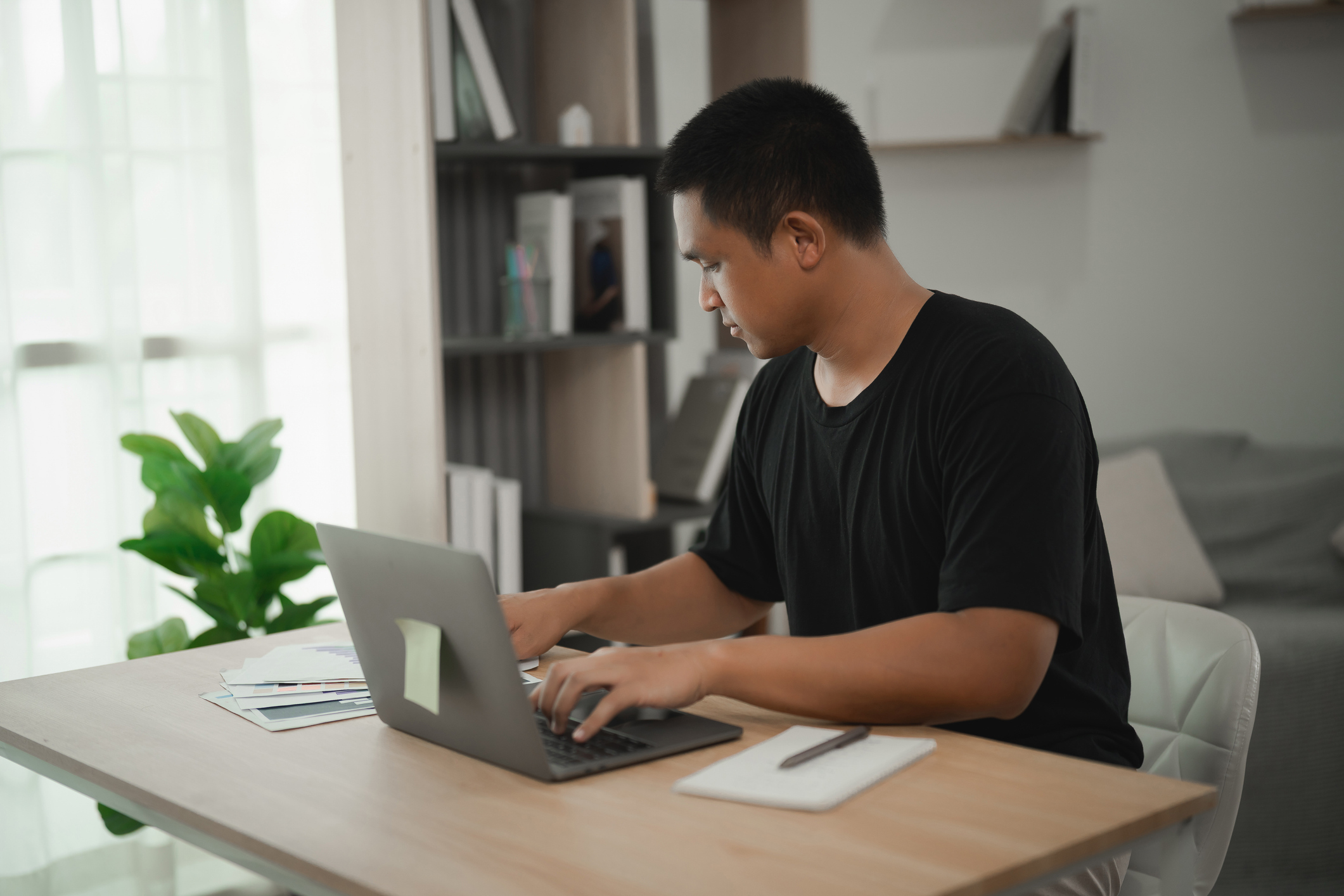 Junger Mann, der an einem Laptop an einem modernen Schreibtisch im hellen Homeoffice arbeitet iStock-2228589750