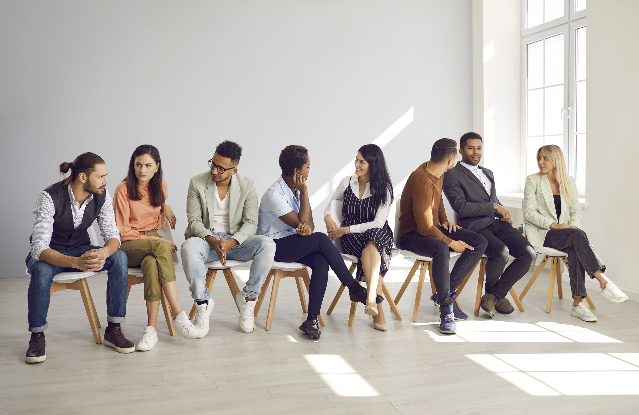bunt gemischte Gruppe , die in einer Sitzreihe sitzt miteinander sprechen iStock-2212131982